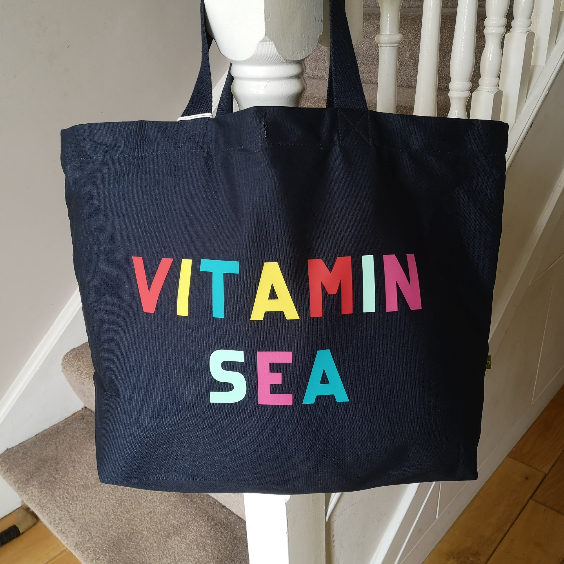 A black organic cotton tote with toggle closing with VITAMIN SEA in different coloured bright lettering on the front