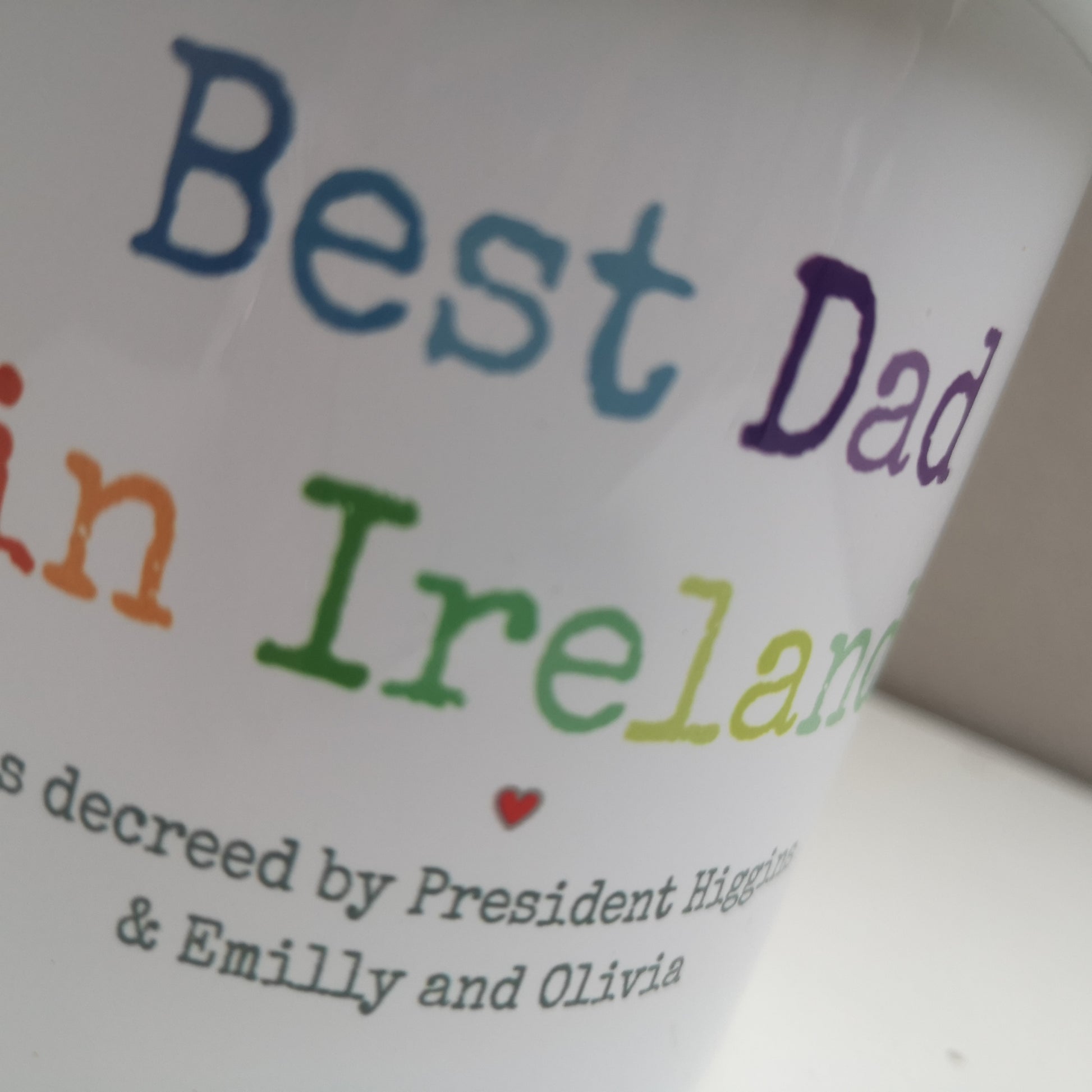 A close up photo of a White enamel mug with a black rim with the following on the front - BEST DAD IN IRELAND, as decreed by President Higgings and personalised names