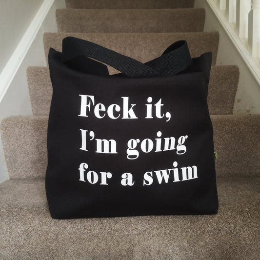A black organic cotton tote with toggle closing with the following text on the front in white type font - FECK IT, I'M GOING FOR A SWIM