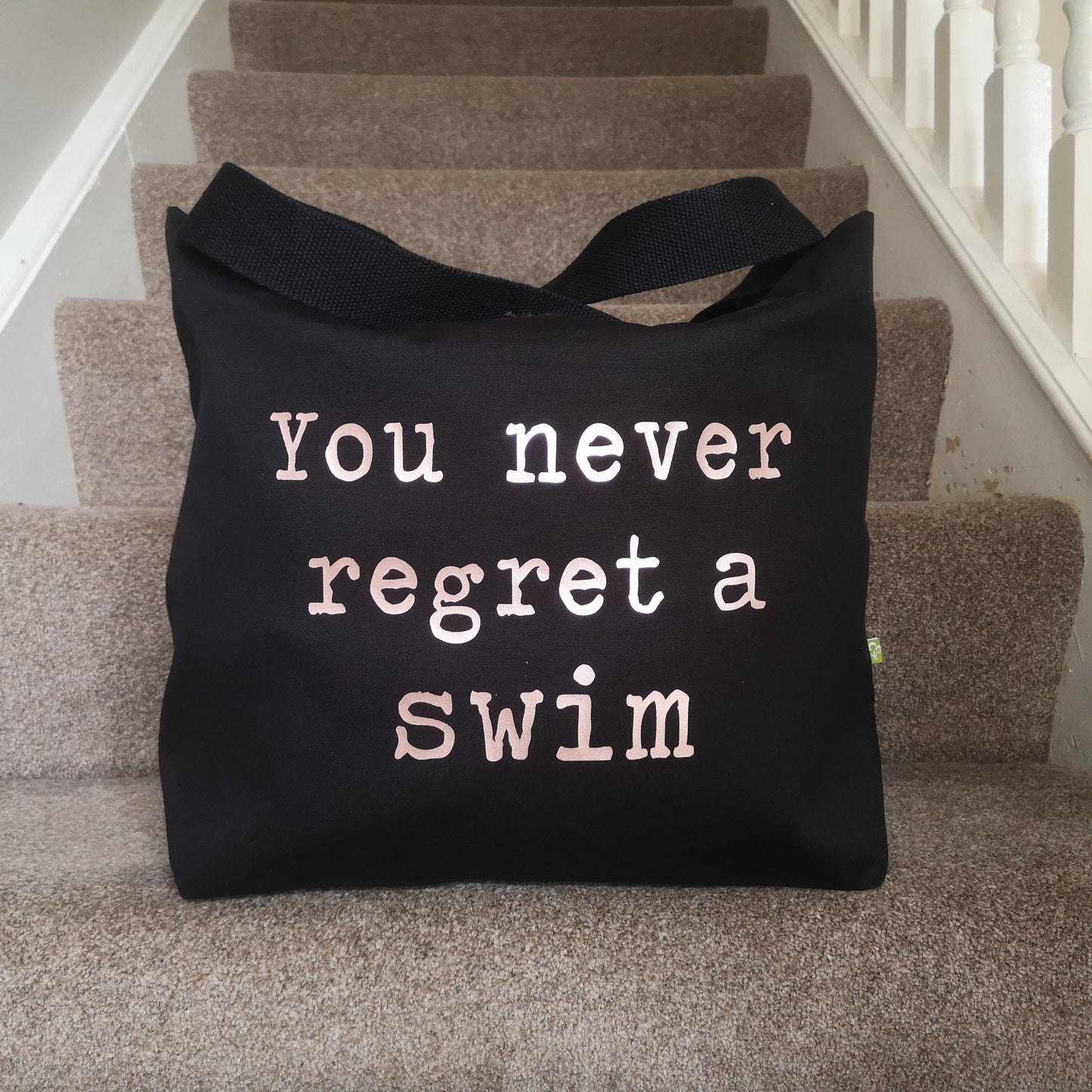 A black organic cotton tote with toggle closing with the following text on the front in white type font - you never regret a swim