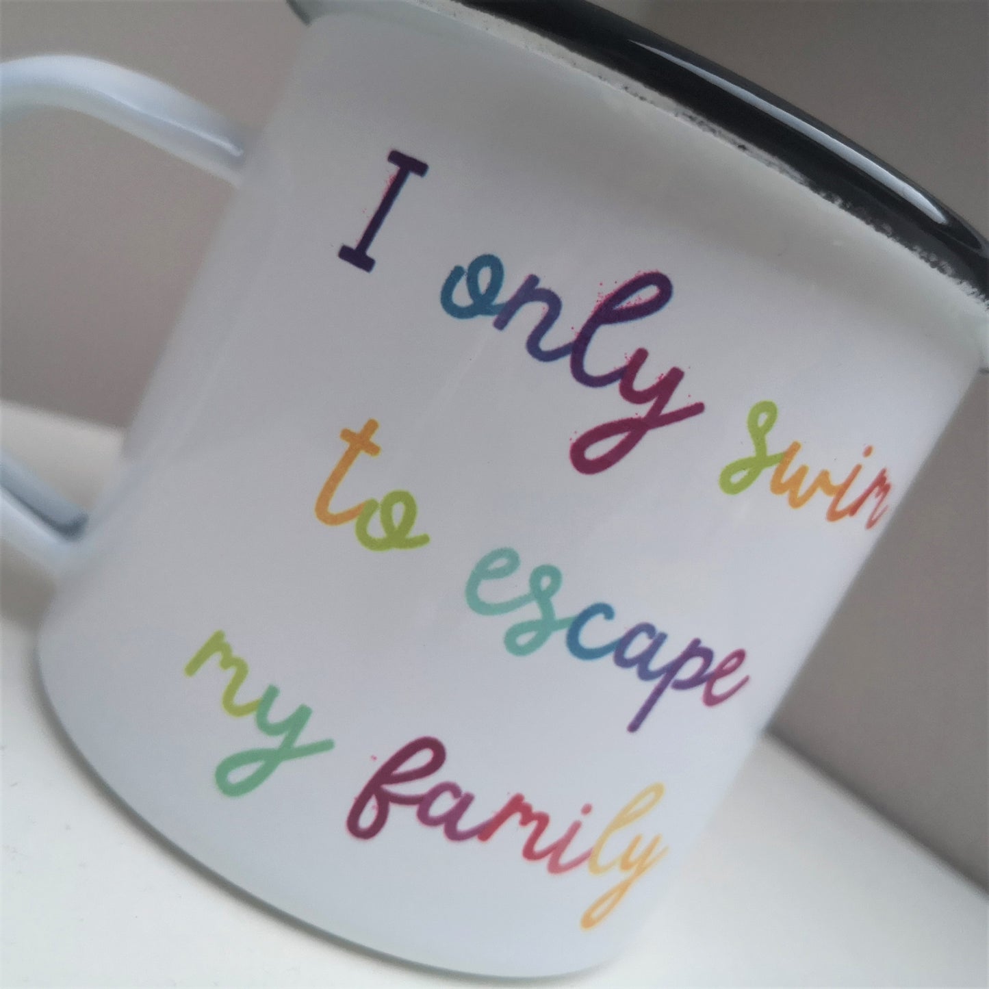 A close up of a steel enamel cup for your after-swim tipples, with a choice of 3 confessions in colourful rainbow text.  This mug has the following excuse - I only swim to escape my family