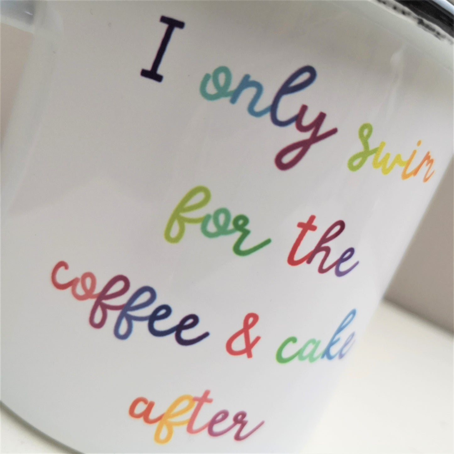 A close up of a steel enamel cup for your after-swim tipples, with a choice of 3 confessions in colourful rainbow text.  This mug has the following excuse - I only swim for the coffee & cake after.  