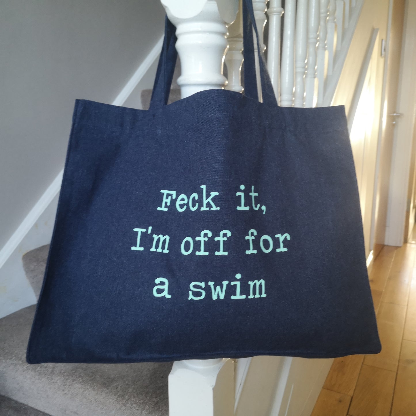 A midnight blue organic cotton tote with toggle closing with the following text on the front in mint green type font - FECK IT, I'M OFF FOR A SWIM 
