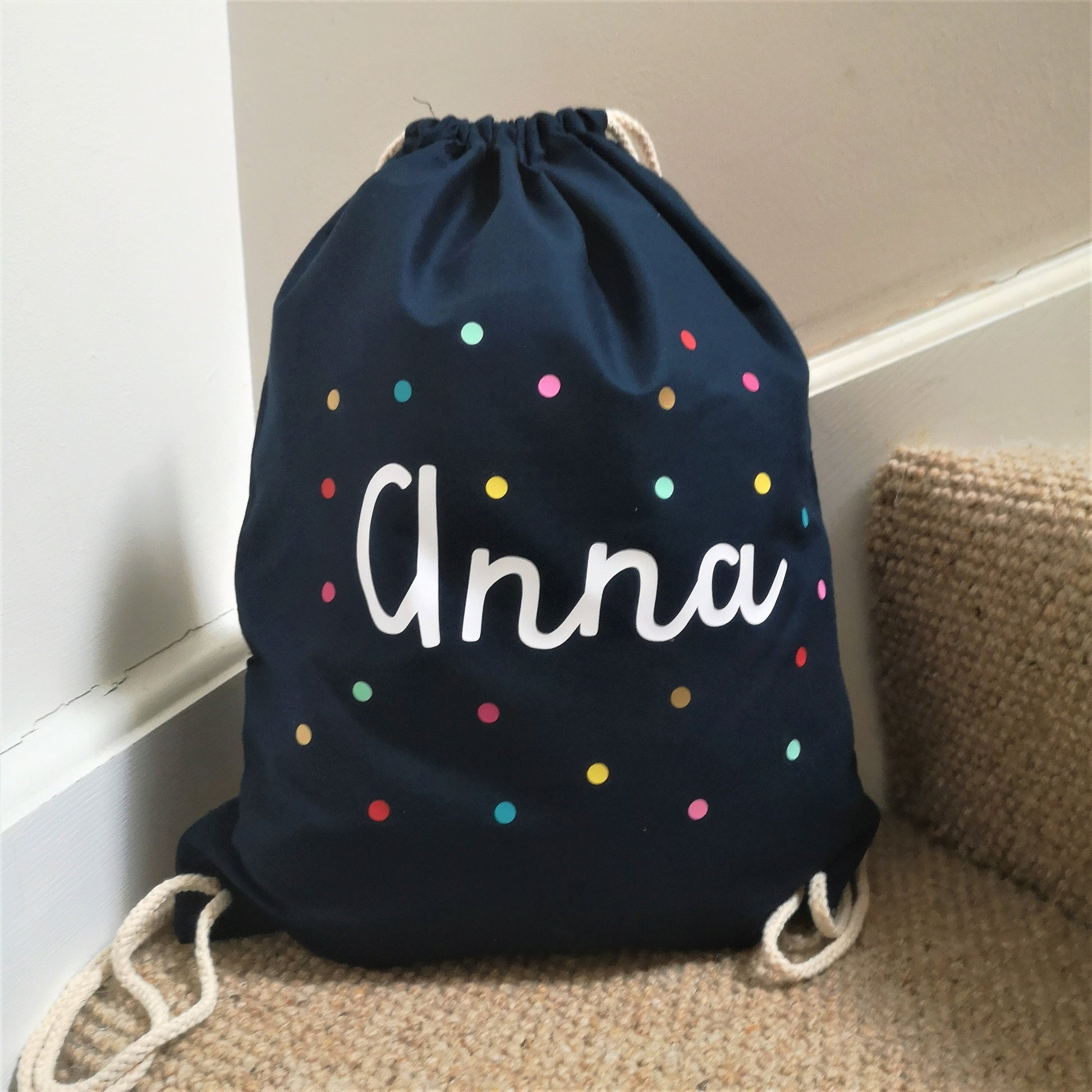 A photo showing the french navy bag colour choice of a personalised light cotton drawstring bag with dots and personalised with a name.  The 3 colour choices are french navy, fuschia pink and light grey