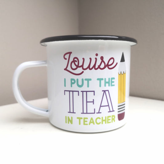 A White enamel mug with a black rim with the following on the front - <NAME> I out the tea in teacher and a big pencil to the right of the text