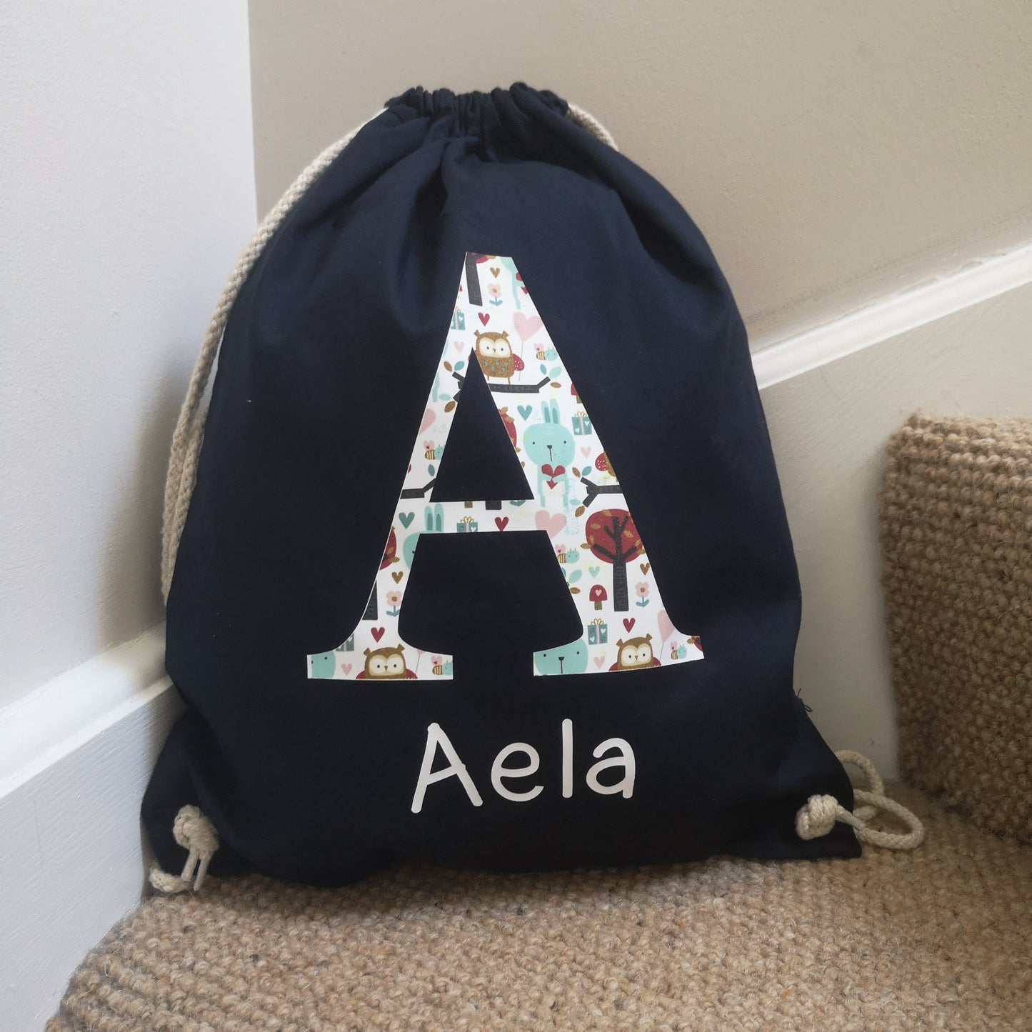 A royal navy personalised light drawstring bag with a patterned Initial and their name underneath