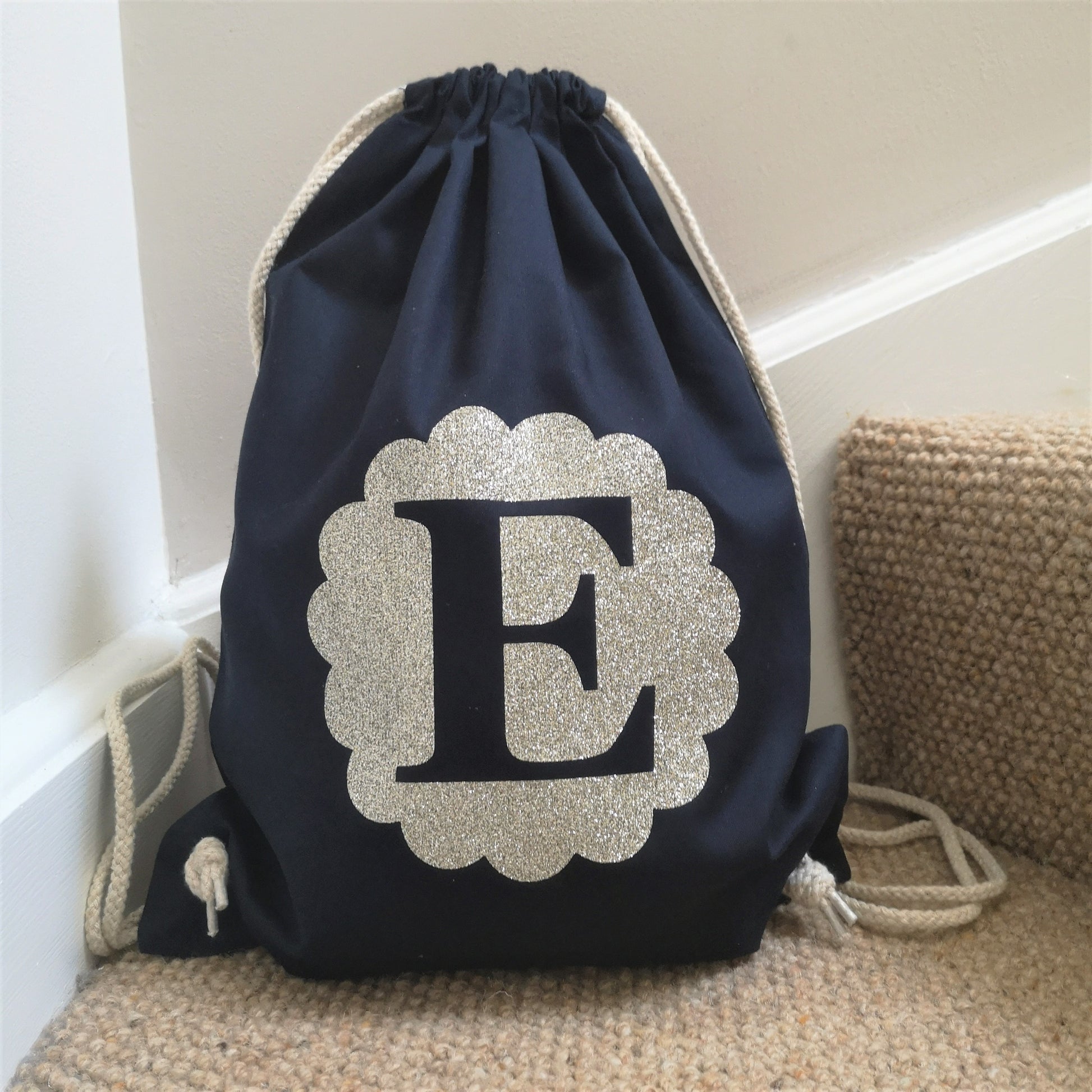 A personalised french navy light cotton drawstring bag with a glittery gold Initial in a scalloped circle on the front of it