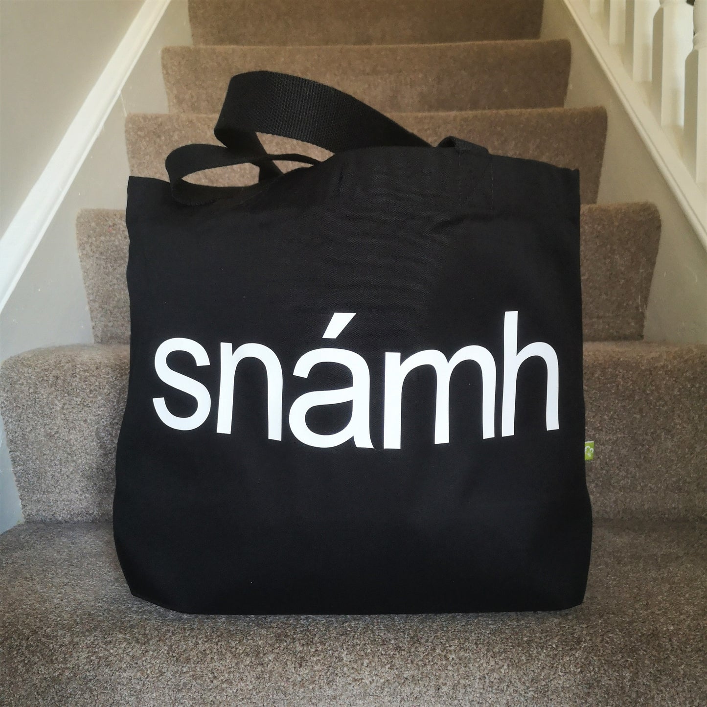 A black organic cotton tote with toggle closing with the following text on the front in white type font - SNÁMH