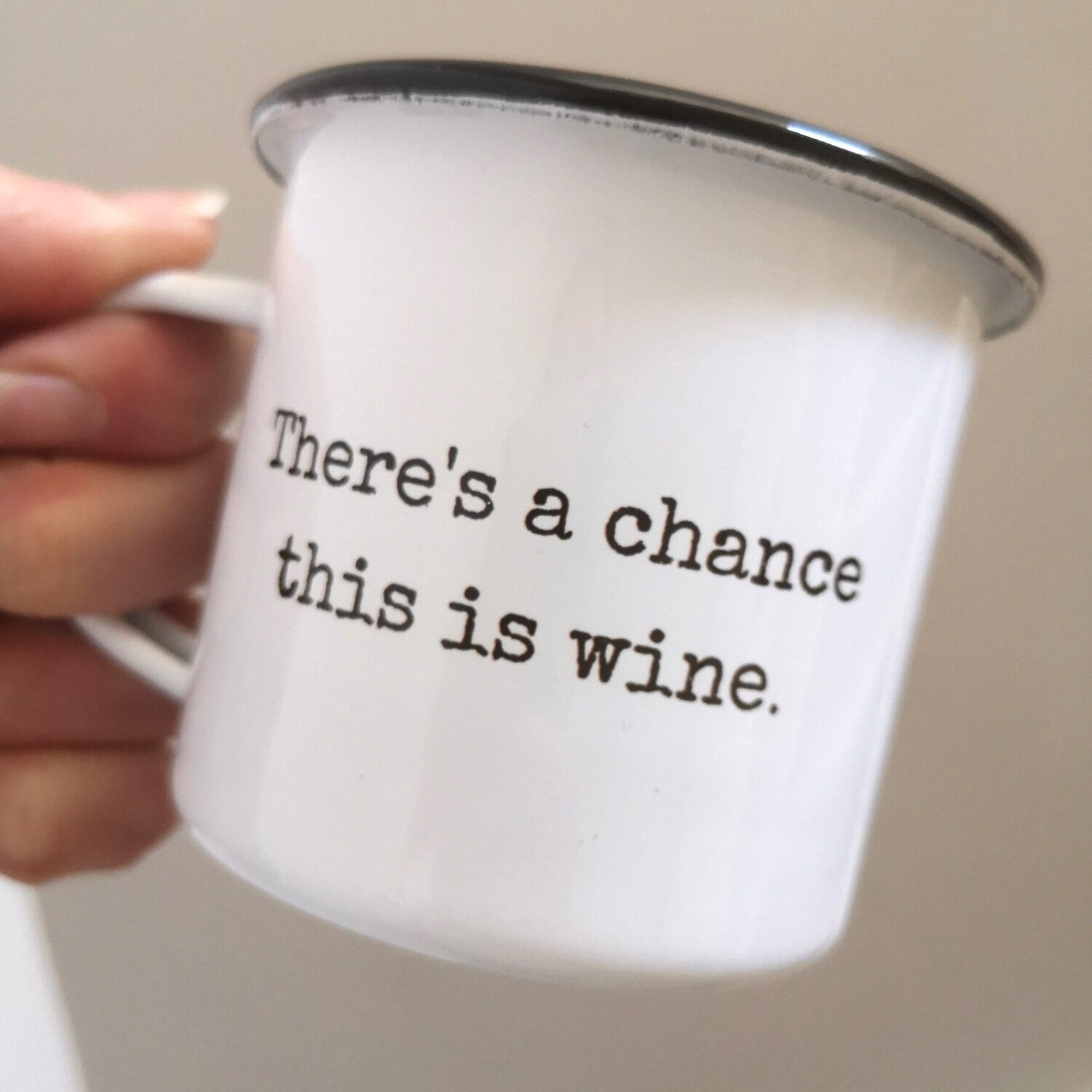 A close up of a White enamel mug with a black rim with the following on the front in black and white lettering - there's a chance this is wine