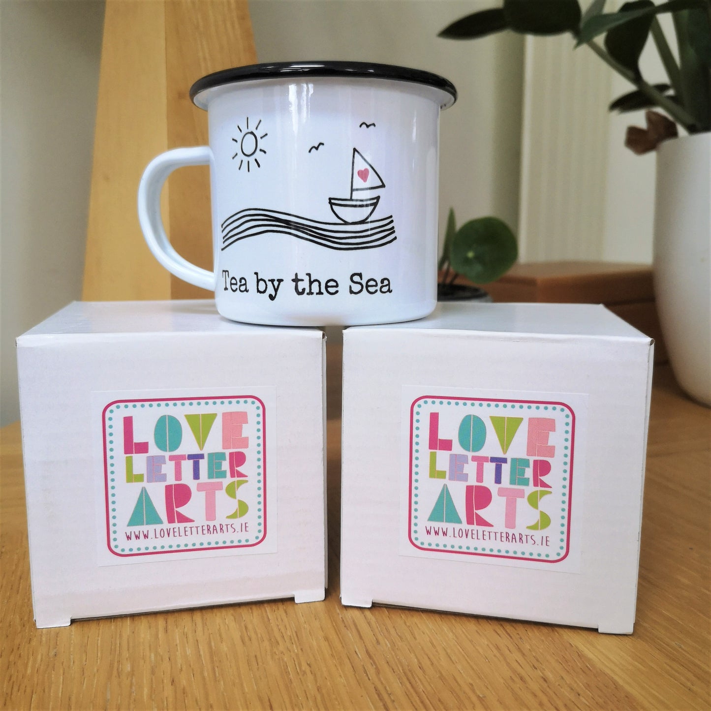A photo showing how I package my mugs. They all come in a white cardboard box with my colourful Love Letter Arts Logo on it.